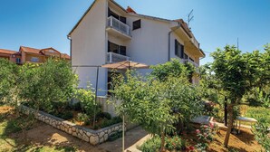 Un bâtiment à deux étages doté d’un balcon, entouré d’un jardin où poussent différentes plantes et fleurs.