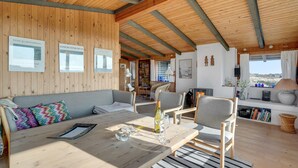 A cozy interior with a wooden ceiling, a sofa with colorful cushions, a dining table with wine glasses, and framed pictures on the wall. - Stunning home in Fanø with WiFi (Fanø)