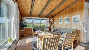 A cozy room with wooden walls and ceiling, a dining table with chairs, a sofa, and a TV on a shelf. - Stunning home in Fanø with WiFi (Fanø)