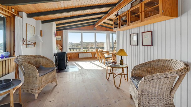 A cozy room with wicker furniture, wooden beams, and large windows offering a view of the hills. - Stunning home in Fanø with WiFi (Fanø)