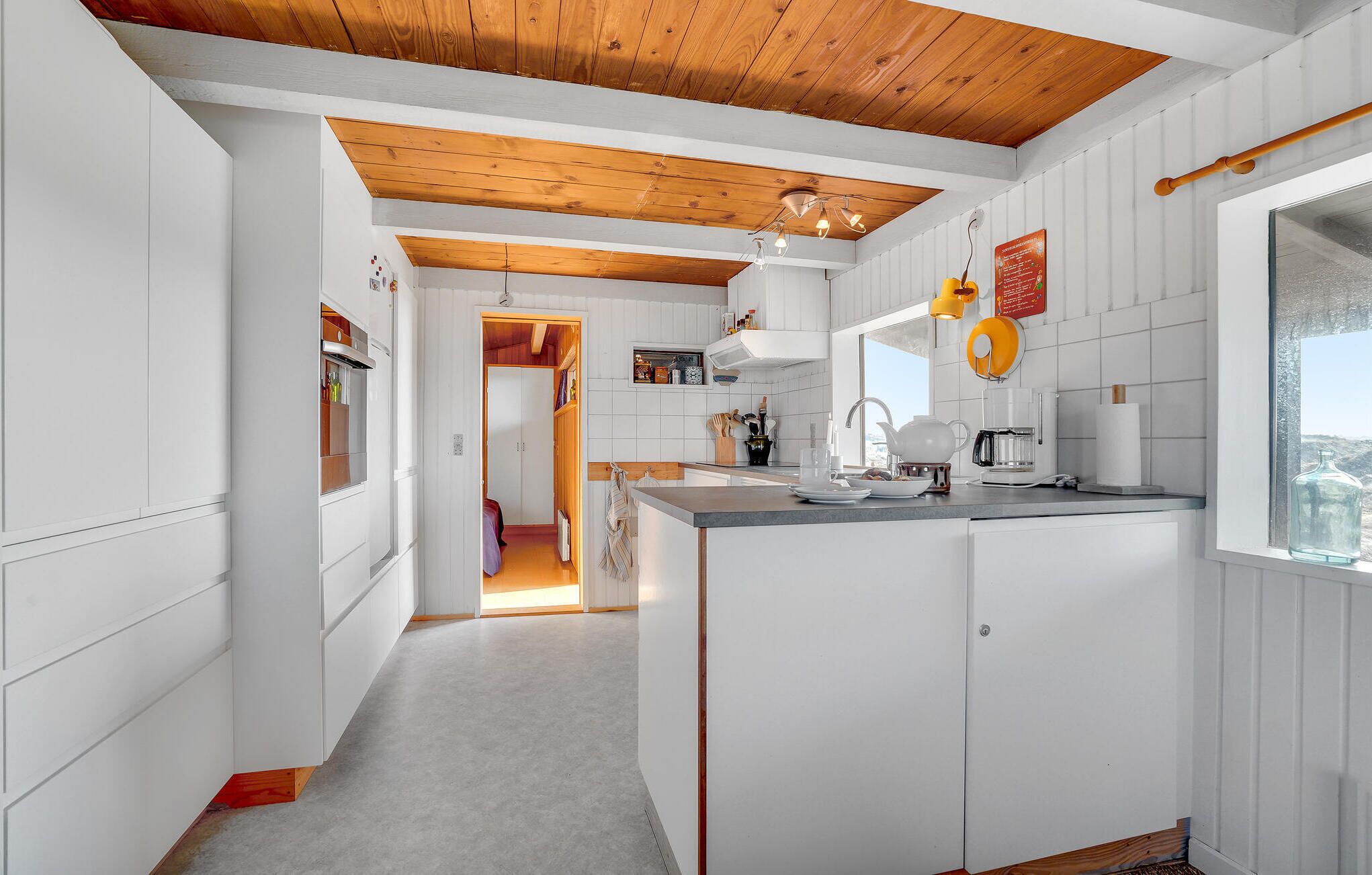 Une cuisine moderne avec des meubles blancs, un plafond en bois et une vue sur l’extérieur par une fenêtre.