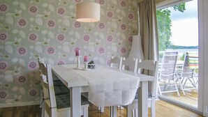 Un comedor con una mesa y sillas blancas, papel tapiz floral y vistas al exterior a través de un ventanal.
