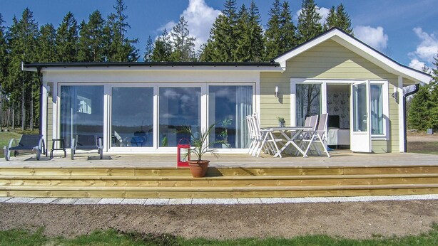 Una casa moderna con grandes puertas de cristal correderas, una terraza con mobiliario exterior y un pequeño porche.