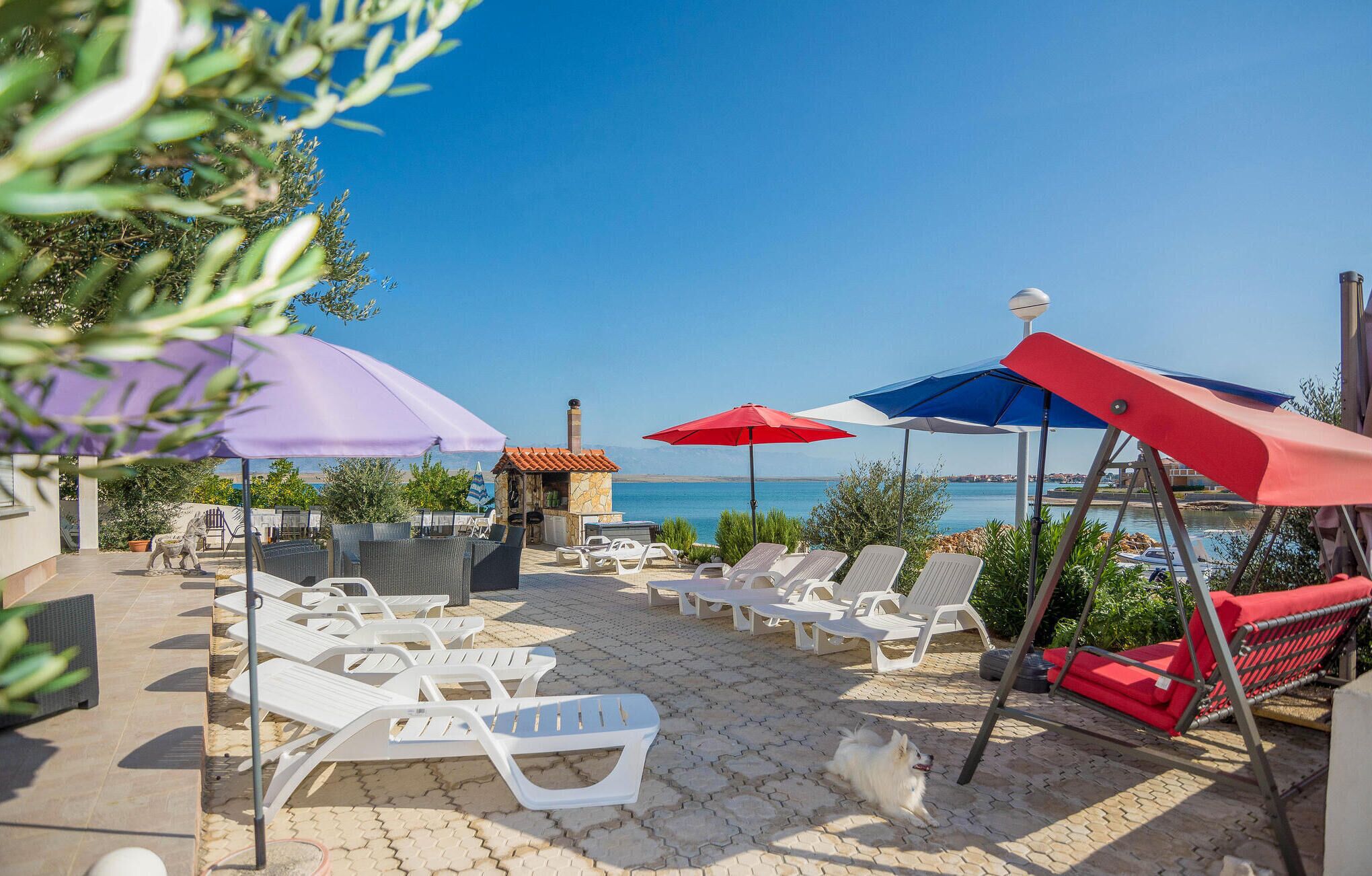 A sunlit outdoor seating area with lounge chairs and umbrellas, overlooking a body of water.