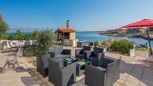An outdoor seating area with wicker furniture, a stone barbecue, and a view of the sea. - Stunning apartment in Vir with house sea view (Vir)