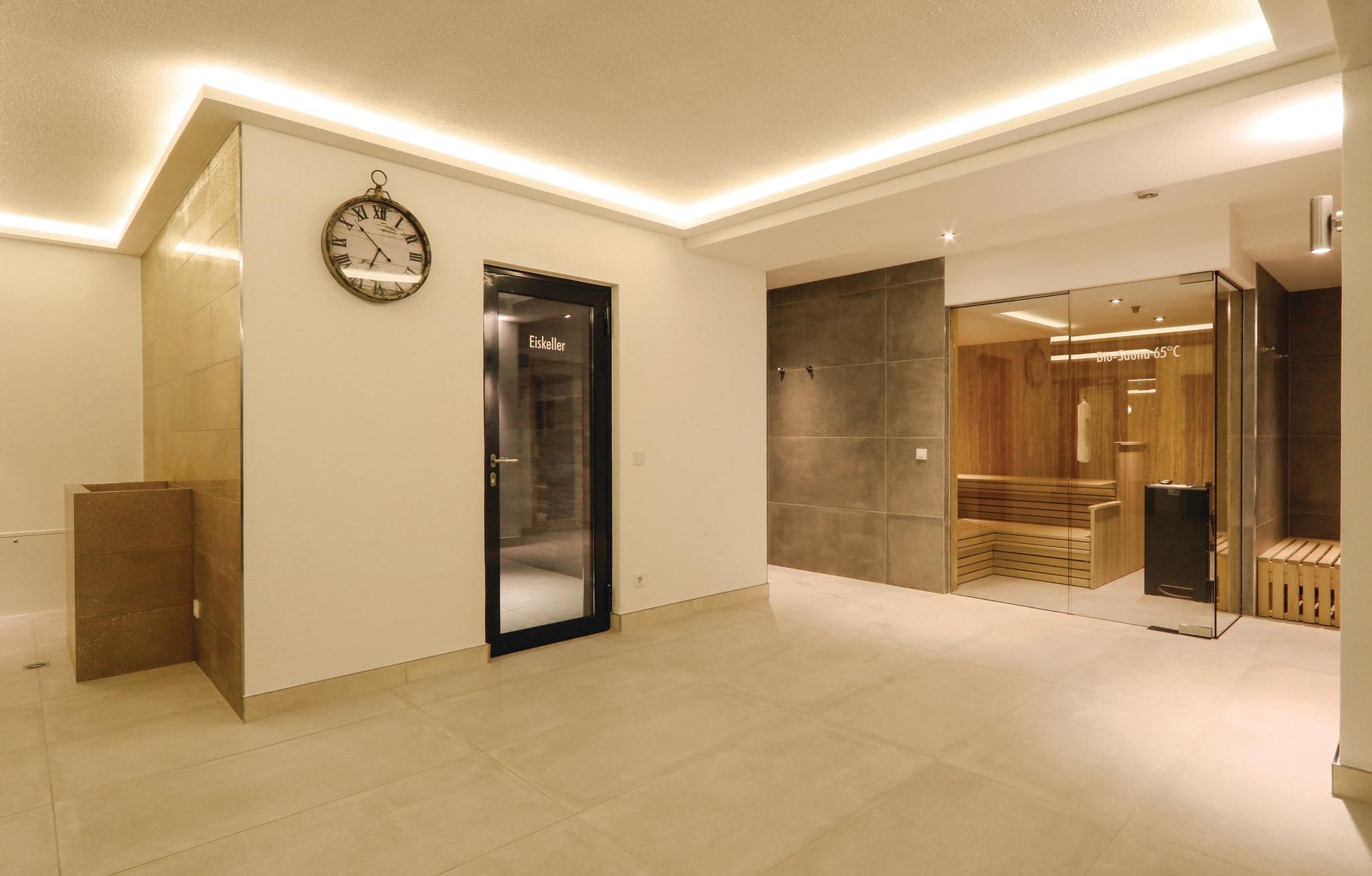 A modern hotel lobby with a minimalist design, featuring a large clock, a reception desk, and a glass elevator.