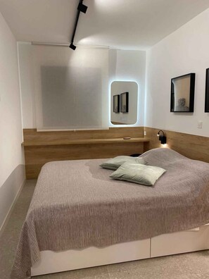 A modern bedroom with a wooden headboard, a bed with striped bedding, a bedside table with a lamp, and wall-mounted artwork. - Holiday apartment with air conditioning and internet (Medulin)