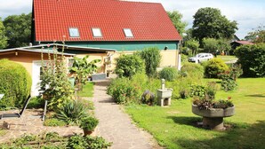 Une maison avec un toit rouge, un jardin avec un chemin, et une voiture garée à proximité.