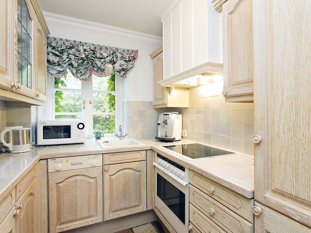 Una cocina con armarios de madera, microondas, tostadora y ventana con cortina estampada.