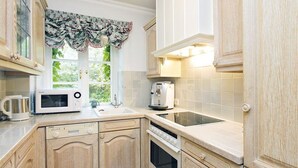Une cuisine avec des meubles en bois, un four à micro-ondes, un grille-pain et une fenêtre ornée d’un rideau à motifs floraux.