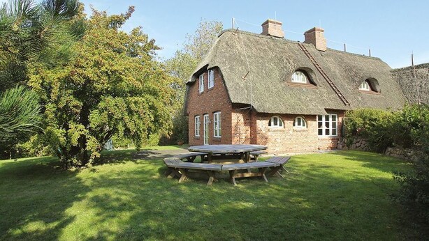 Une maison traditionnelle en briques, avec un toit de chaume, une table de pique-nique en bois et une pelouse bien entretenue.