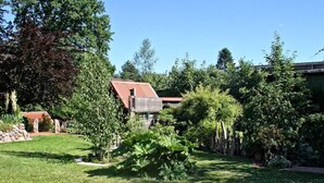 A well-maintained garden with a variety of trees and shrubs, a stone wall, and a house with a red roof. - Heisch: Cozy vacation home with terrace and beach chair - Ferienhaus Heisch (Schafflund)