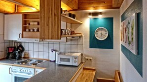 A kitchen with wooden cabinets, a microwave, a stove, and a clock on the wall. - Heisch: Cozy vacation home with terrace and beach chair - Ferienhaus Heisch (Schafflund)