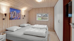 Ein Schlafzimmer mit Holzwandverkleidung, einem Bett mit weißer Bettwäsche, einem Stadtbildgemälde, einem Fenster mit Ausblick und einem an der Wand montierten Fernseher.