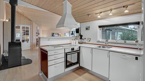 Eine moderne Küche mit weißen Schränken, einem Einbauofen, einer Spülmaschine und einem großen Fenster mit Blick ins Freie.