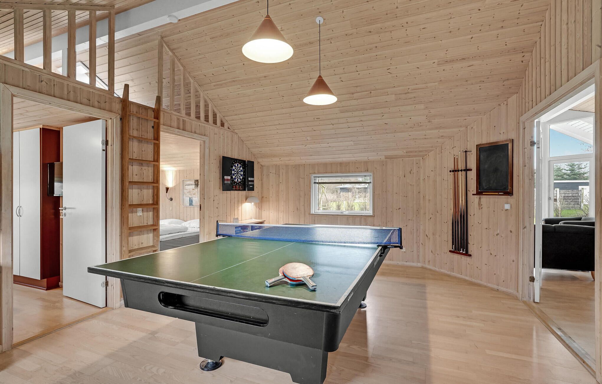 A ping pong table in a room with wooden walls and ceiling, a window, and a door leading to another room.