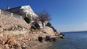 A coastal building with a stone facade, a balcony, and a staircase leading to the entrance. - Holiday apartment near the sea (Barić Draga)