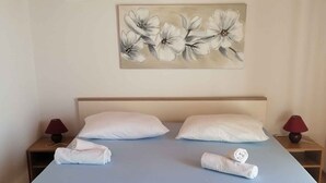 A neatly made bed with white linens and towels, a wooden headboard, and a floral painting on the wall. - Holiday apartment near the sea (Barić Draga)