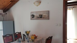 A dining area with a wooden ceiling, a table with a floral tablecloth, four chairs, and a wall-mounted picture of coffee cups. - Holiday apartment near the sea (Barić Draga)