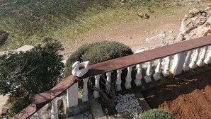 A clear view of a large body of water, likely a lake or sea, with a rocky shoreline and a railing in the foreground. - Holiday apartment near the sea (Barić Draga)