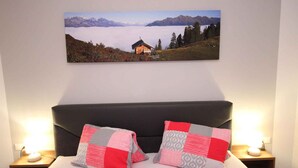 Een bed met een sprei, twee bedlampjes en een wanddecoratie van een berglandschap.