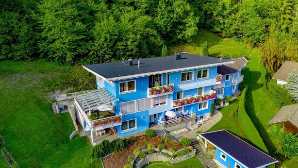 Een meerlaags blauw gebouw met balkons, omgeven door weelderige begroeiing.