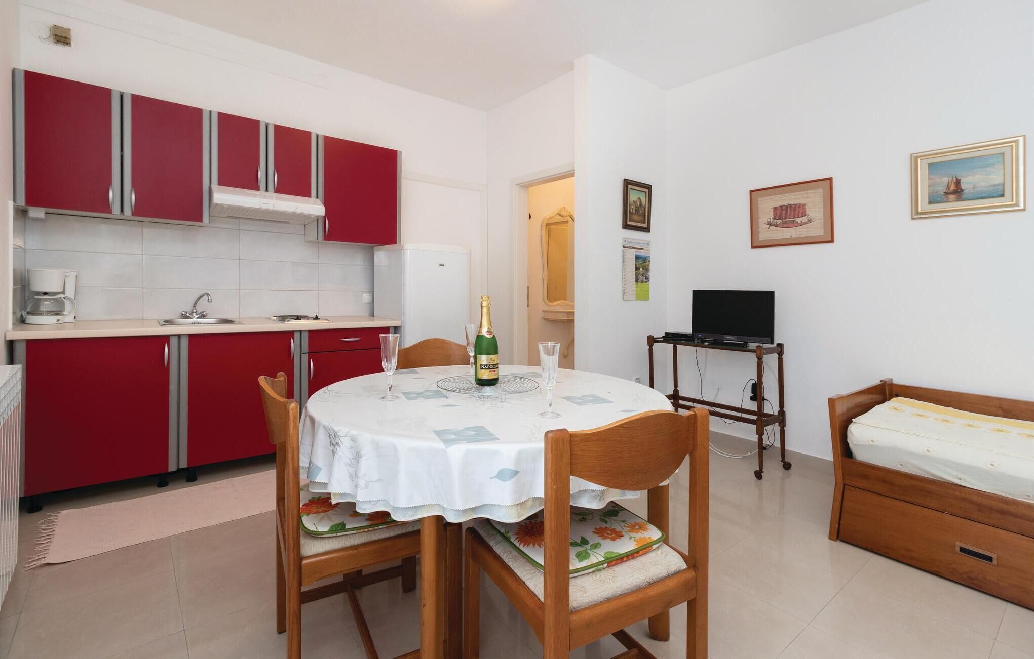 Un espacio habitable compacto con kitchenette, una zona de comedor con mesa y sillas, un televisor sobre un mueble y una cama.