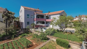 A multi-story building with a red-tiled roof, a balcony, and a garden area with various plants and a pathway. - Amazing apartment in Zadar with WiFi (Zadar)