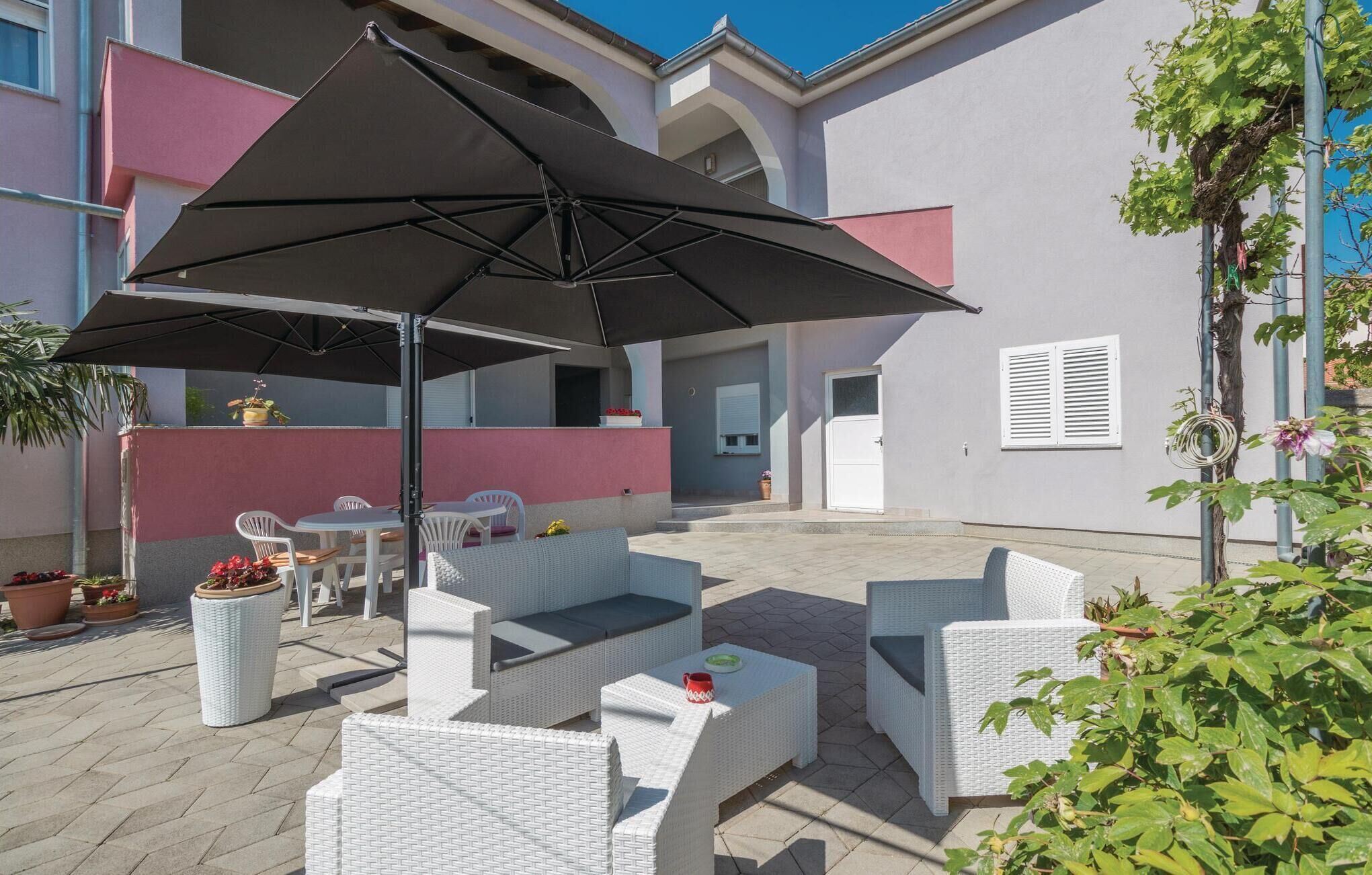 An outdoor patio area with white wicker furniture, a large black umbrella, and potted plants.