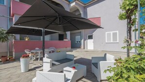 An outdoor patio area with white wicker furniture, a large black umbrella, and potted plants. - Amazing apartment in Zadar with WiFi (Zadar)
