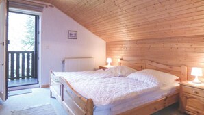 A wooden bedroom with a bed, two bedside lamps, a radiator, and a door leading to an outdoor balcony. - Ferienhaus 18 in Thalfang (Thalfang)