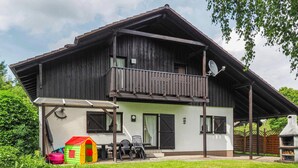 A two-story wooden house with a balcony, a patio with a table and chairs, and a small playhouse. - Ferienhaus 18 in Thalfang (Thalfang)