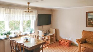 Ett rum med ett matbord och stolar i trä, en tv som är monterad på väggen, ett fönster med gardiner och en brun lädersoffa.