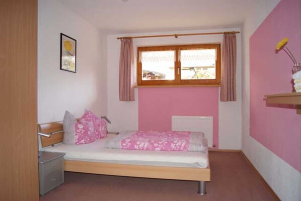 Een slaapkamer met een bed, nachtkastje en een raam met gordijnen.