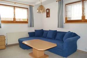 A room with a blue sofa, a wooden coffee table, a wicker basket, and a wall clock.