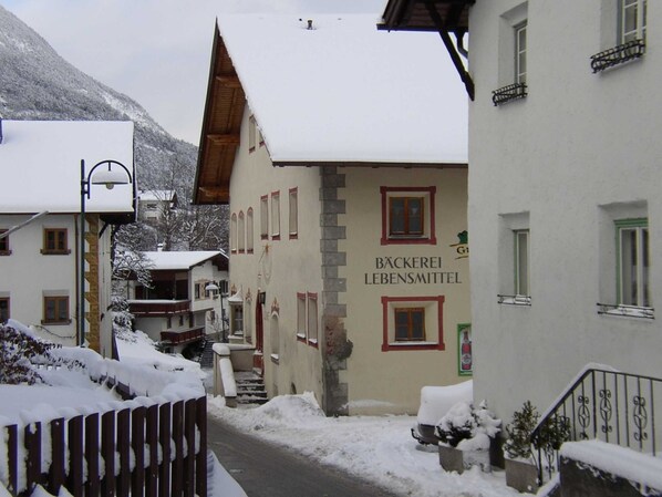 A snow-covered street with buildings, including one labeled 'BÄCKerei Lebensmittel.'