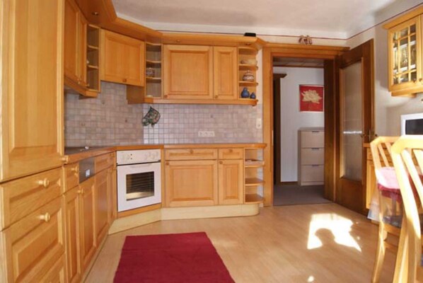 A kitchen with wooden cabinets, a tiled backsplash, a red rug, and a doorway leading to another room.