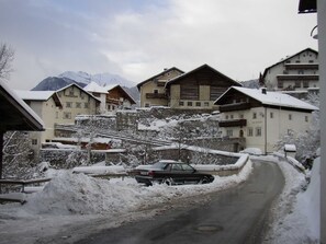 A snow-covered village with traditional chalet-style buildings, a winding road, and mountains in the background. - Apartment Ursula - Apartment 1 (Grins)