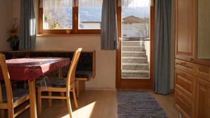 Una habitación con mesa de comedor, sillas, una ventana con cortinas, una escalera y armarios de madera.