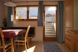 Una habitación con mesa de comedor, sillas, una ventana con cortinas, una escalera y armarios de madera.