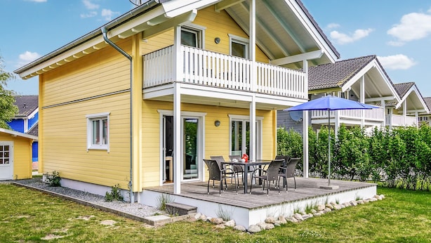Een geel huis met een balkon, een terras met buitenmeubilair en een schotelantenne.