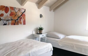 Un dormitorio con dos camas, una mesita de noche con una planta, una lámpara de pared y un cuadro de hojas otoñales.