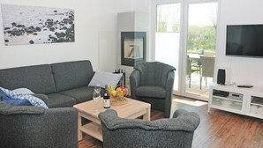 Een moderne woonkamer met grijze meubels, een houten salontafel met een wijnfles en fruit, en een televisie op een witte kast.