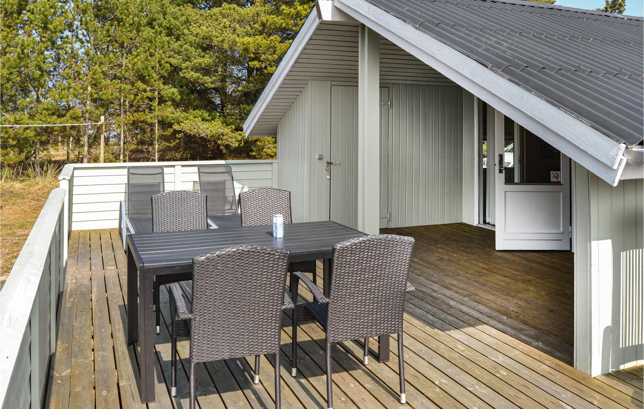 Un espacio comedor al aire libre con techo, una mesa, sillas, una terraza de madera y un edificio blanco con tejado gris.