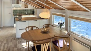 Una cocina acogedora con una mesa y sillas de madera, una lámpara colgante y vistas a un paisaje nevado a través de las ventanas.