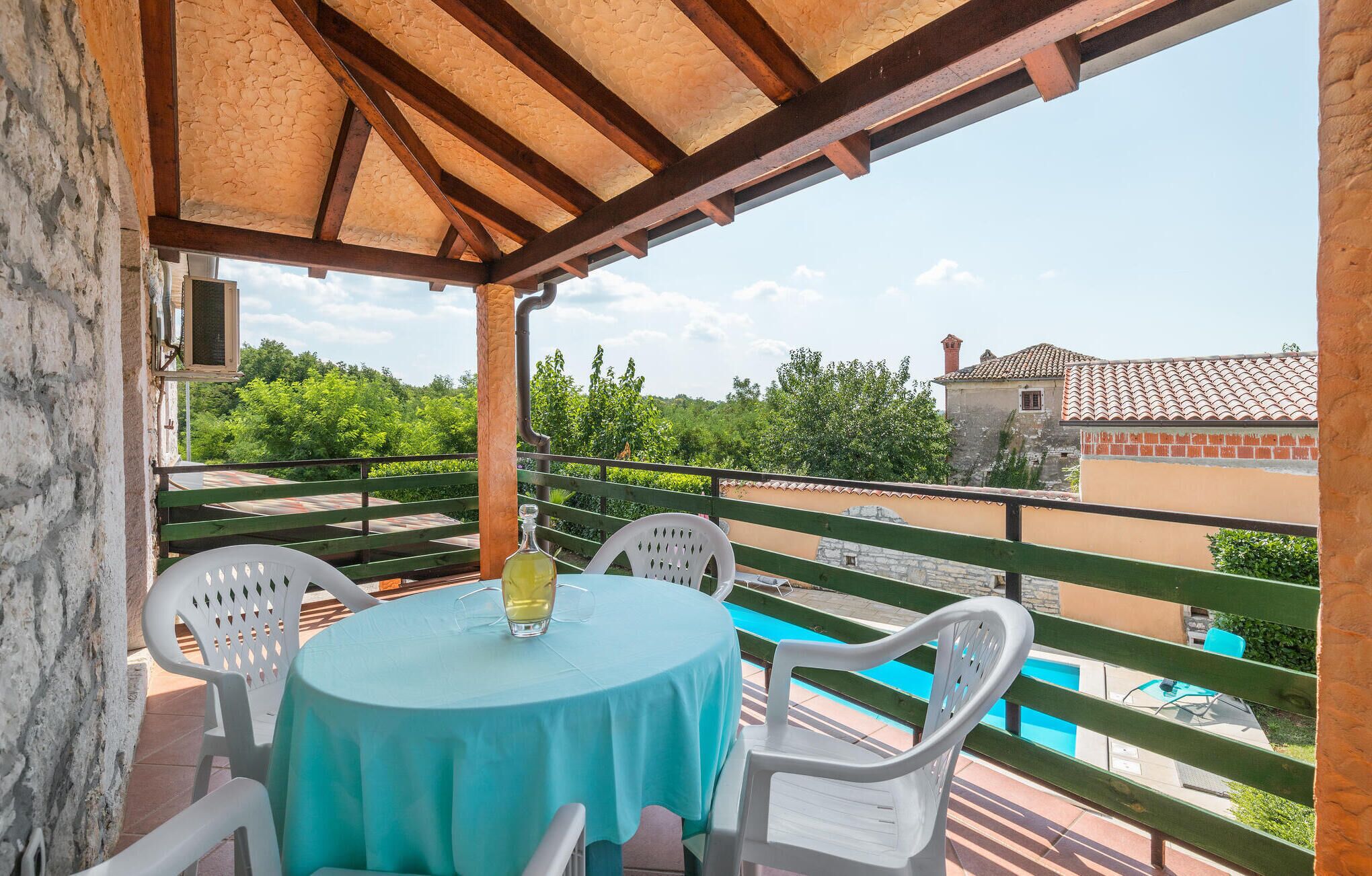A covered outdoor seating area with a table and chairs, overlooking a swimming pool and greenery.