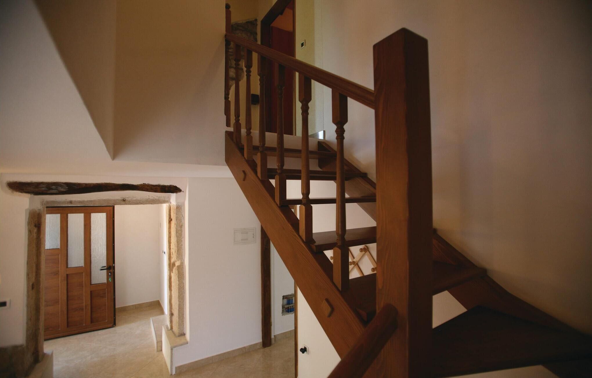Eine Holztreppe mit Handlauf führt zu einer oberen Etage. Am Fuß der Treppe ist eine Tür mit Glasscheiben zu sehen.