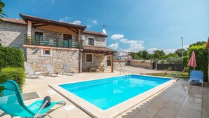 Une maison en pierre à deux étages, dotée d’une piscine, d’un espace salon extérieur et d’un patio couvert.