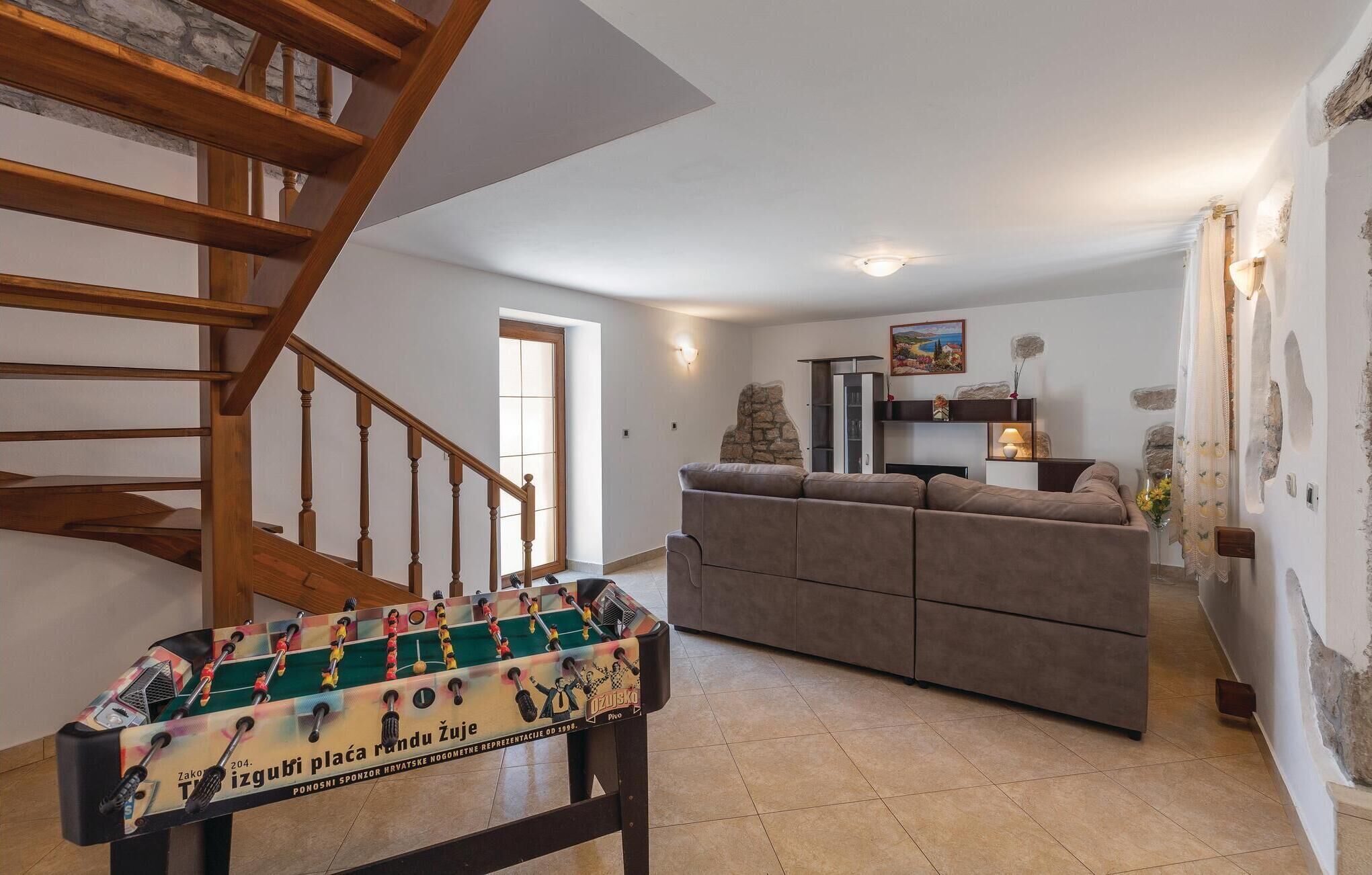 A living room with a sofa, a foosball table, and a wooden staircase.