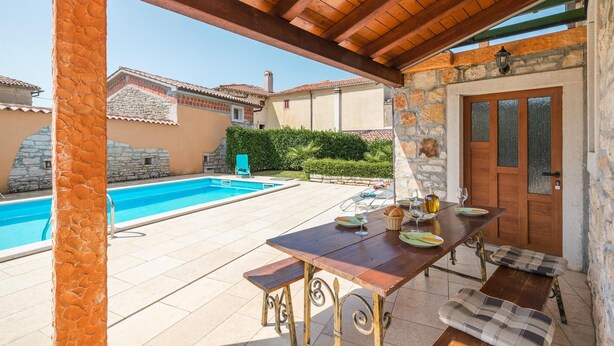 Un espace extérieur abrité comprenant une piscine, une table en bois avec des chaises et une porte.